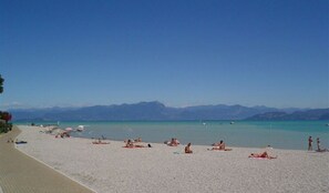 A beach with people sunbathing and swimming, a clear sky, and mountains in the background.