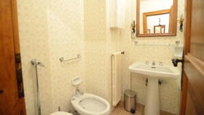 Een badkamer met toilet, bidet, wastafel, spiegel en een handdoekradiator.