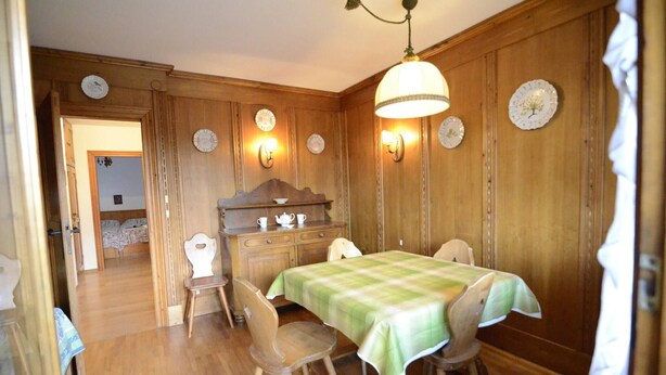 Een eetkamer met een houten tafel voor vier personen, een houten kast met decoratieve borden en een kroonluchter.