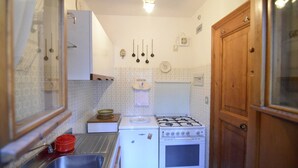 Een compacte keuken met een gasfornuis, een kleine koelkast en een spoelbak.