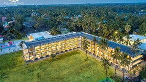 A resort with a large building, a grassy courtyard, and palm trees. - The Village Resort (Ngwe Saung)