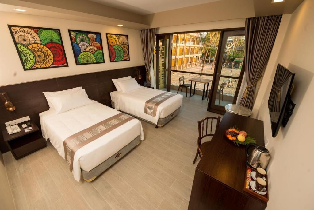 A hotel room with two beds, a desk with a coffee maker, and artwork on the walls.
