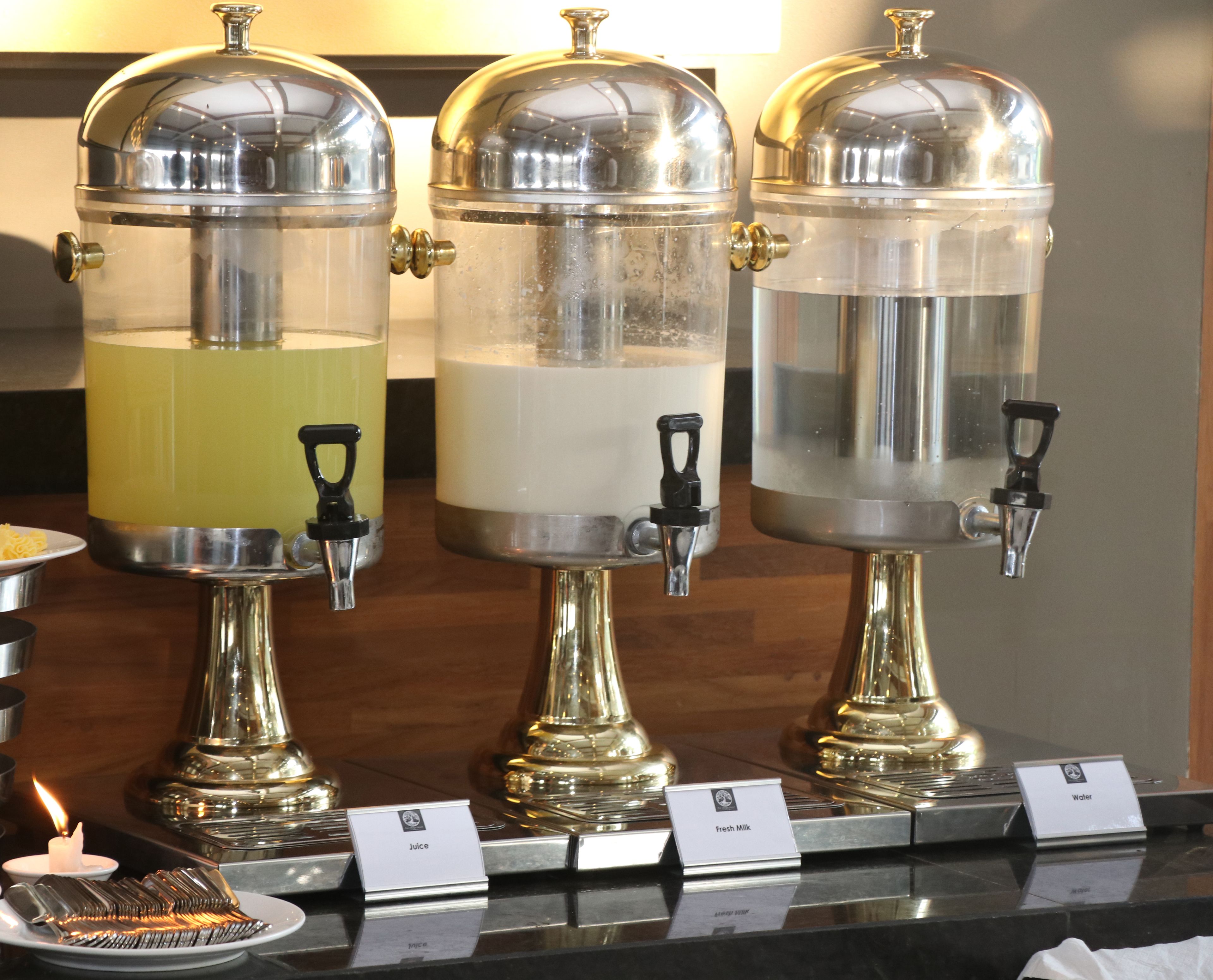 Three beverage dispensers with spigots, each labeled with a different drink: juice, fresh milk, and water.