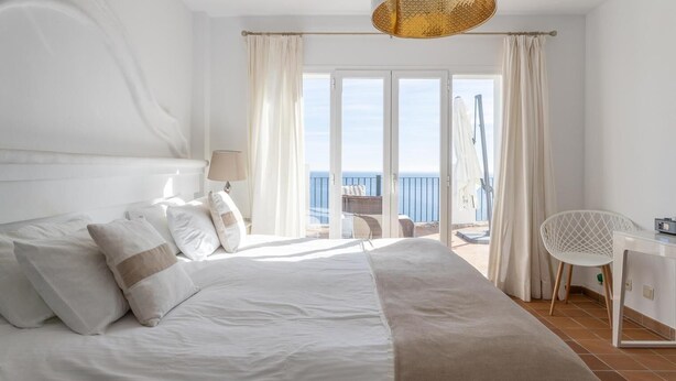 A bedroom with a large bed, a desk, and a view of the sea.