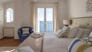 A hotel room with a bed, a chair, a view of the sea, and a balcony.