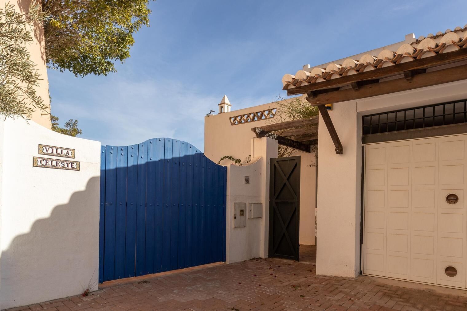 Een omheind toegangspunt tot een landgoed genaamd "Villa Celeste", met een blauwe poort, een witte garageklep en een pannendak.