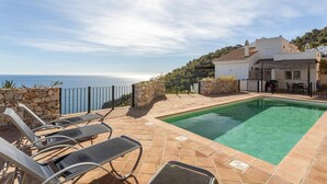 A pool area with lounge chairs, a stone wall, and a view of the sea.