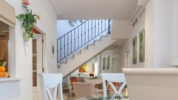 A modern interior with a glass dining table, white chairs, a staircase, and a kitchen area visible in the background. - Spectacular apartment with private terrace / WIFI (Sevilla)