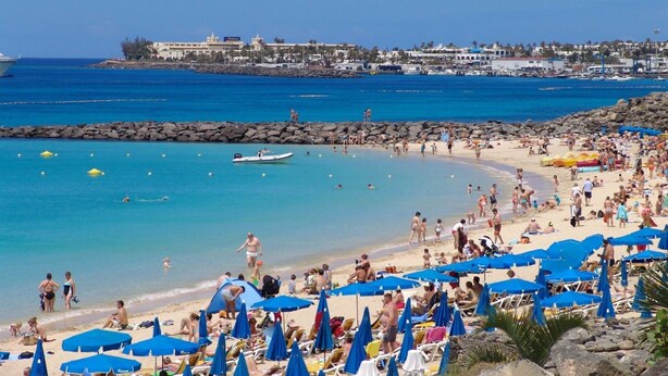 Platja concorreguda amb nombrosos paraigües blaus i gent gaudint del sol.