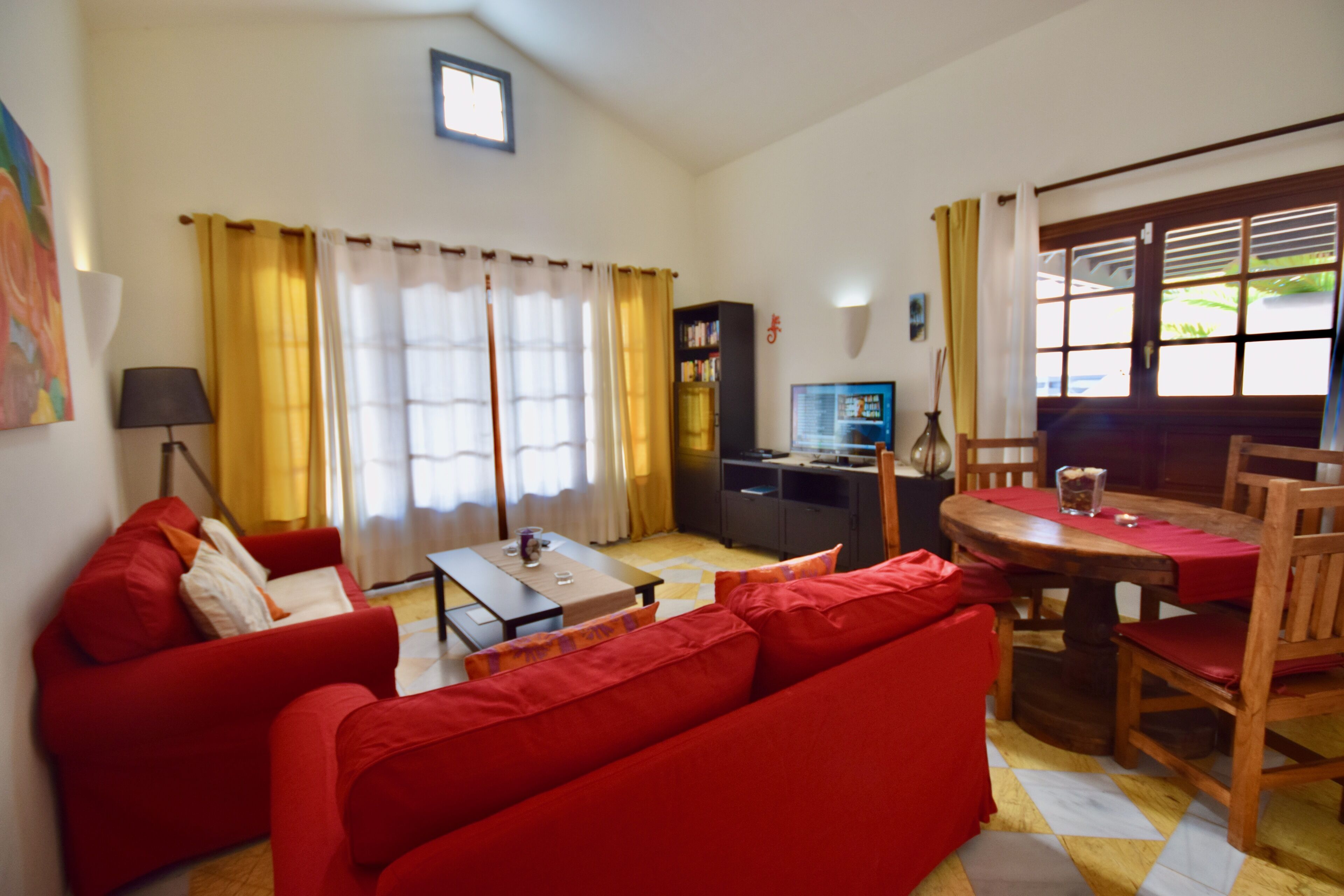 A living room with a red sofa, a wooden dining table, and a TV.