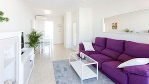 A modern living room with a purple sofa, white coffee table, and a glass-top table. - Beautiful property with 2 bedrooms. Swimming pool. Wifi - only families (Playa de Gandía)