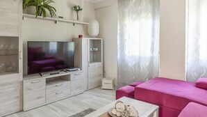 A modern living room with a flat-screen TV, a pink sofa, and a coffee table with decorative items. - Live the most authentic Seville TRIANA ↑ Qualities (Sevilla)