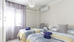 A hotel room with two beds, a ceiling light, an air conditioner, and a window with curtains. - Live the most authentic Seville TRIANA ↑ Qualities (Sevilla)