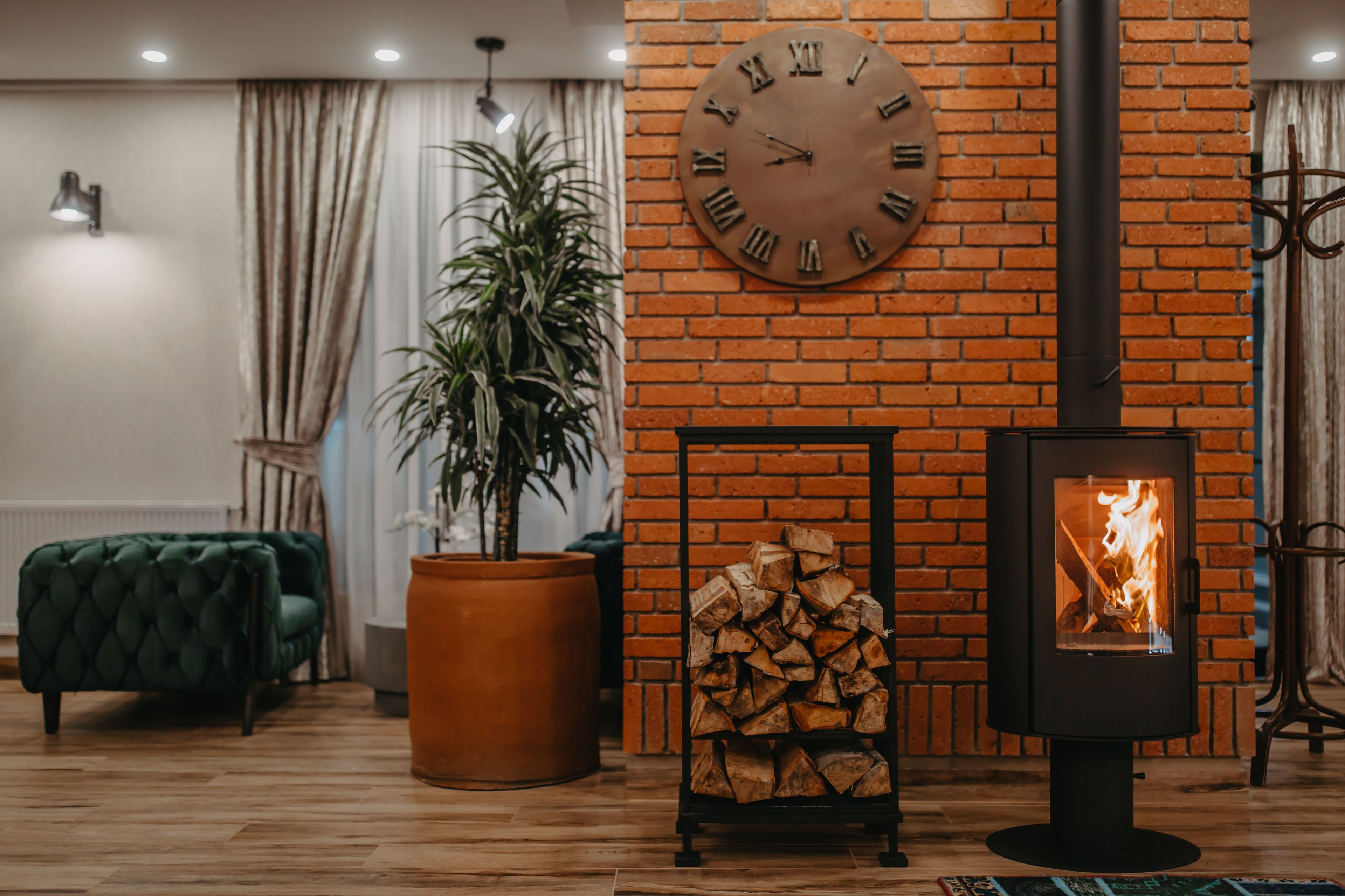 Un salon chaleureux avec un mur en briques, une grande horloge, un poêle à bois, un canapé vert et une plante en pot.
