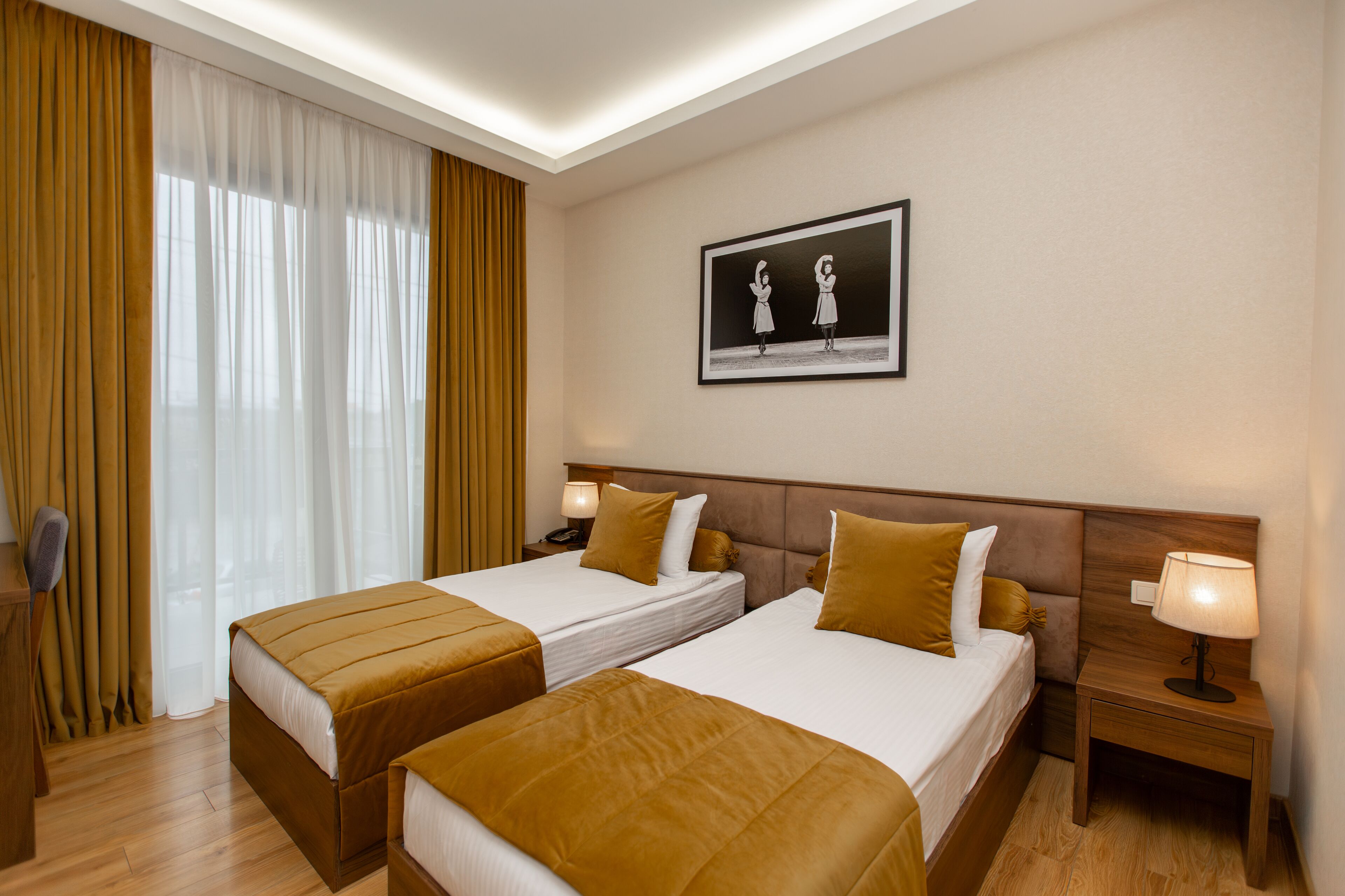 A hotel room with two beds, a nightstand with a lamp, a framed picture on the wall, and a window with curtains.