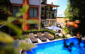 A rooftop pool with lounge chairs, a dining area, and a view of a multi-story building with balconies. - Seventeen Rooms (Telavi)