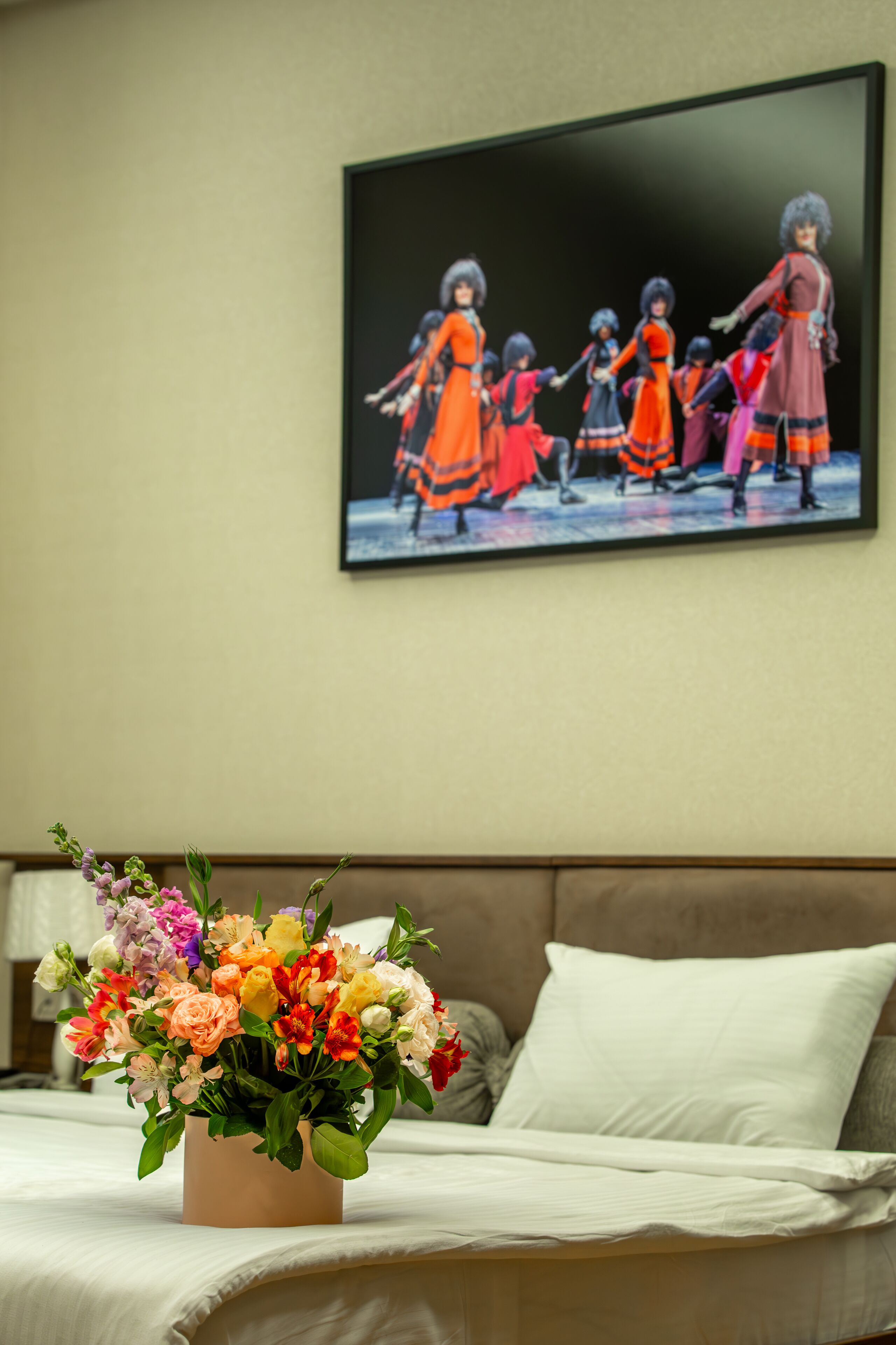A bedroom with a bed, a floral arrangement on the bed, and a painting on the wall.