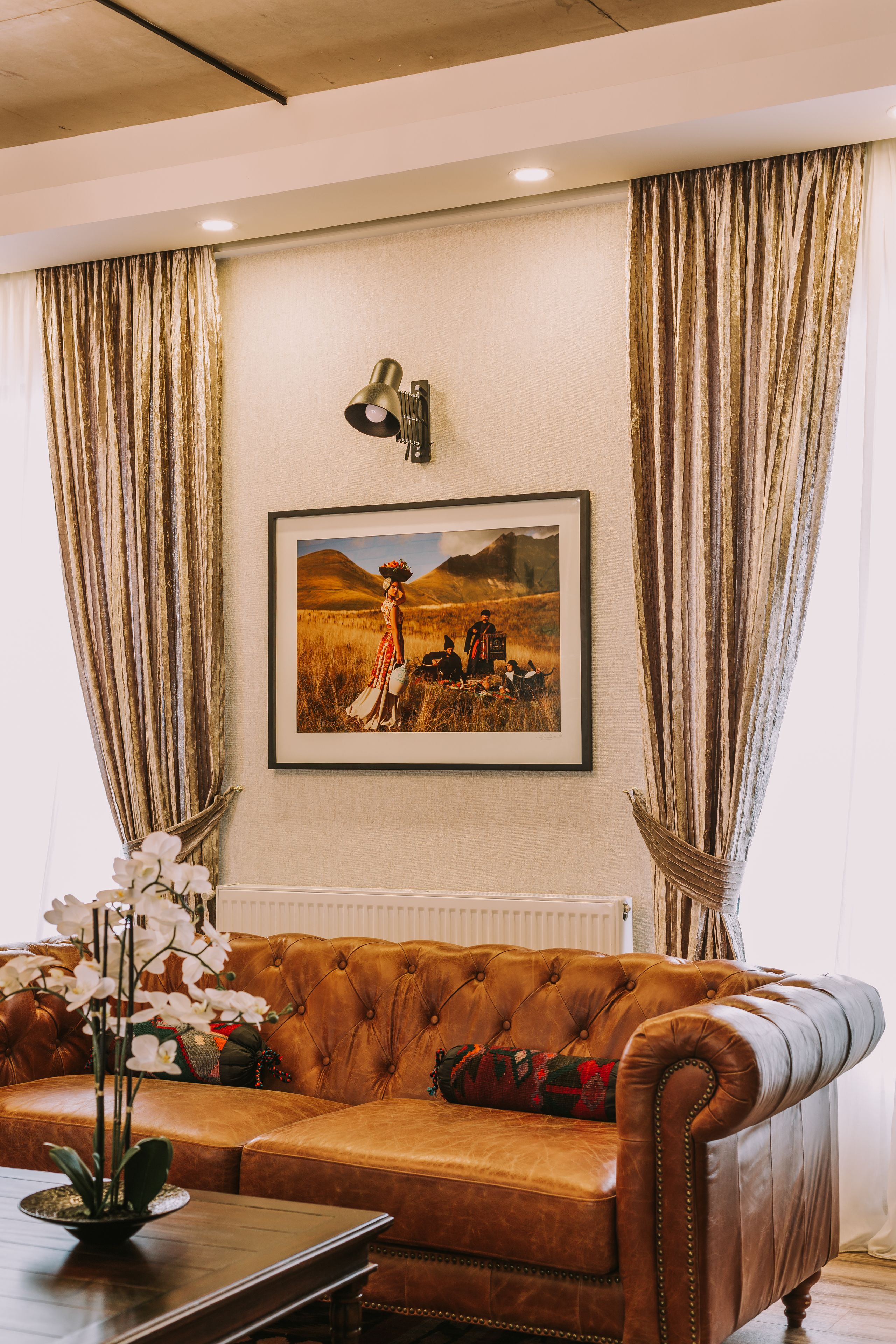 A brown leather sofa with a framed picture above it, a small table with a plant, and a radiator below.