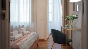 A hotel room with a bed, a desk with a vase of flowers, and a door leading to another room. - Wine Apartments Florence Moscato (Florence)