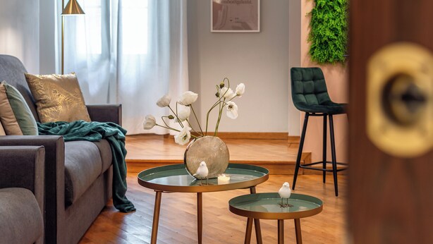A modern living room with a sofa, two round glass tables, a green chair, and a wall-mounted plant. - Wine Apartments Florence Moscato (Florence)