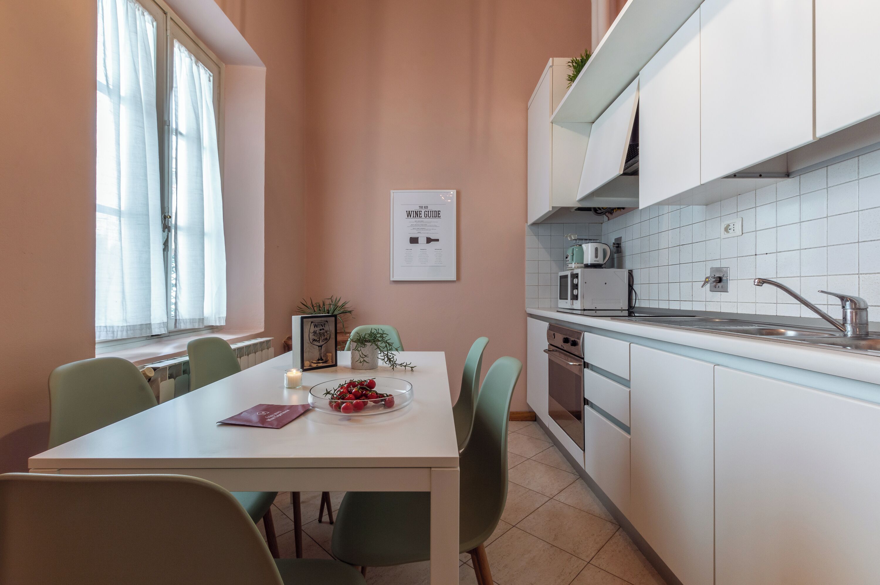 Une cuisine moderne avec des meubles blancs, un plan de travail blanc et une fenêtre ornée de rideaux légers.