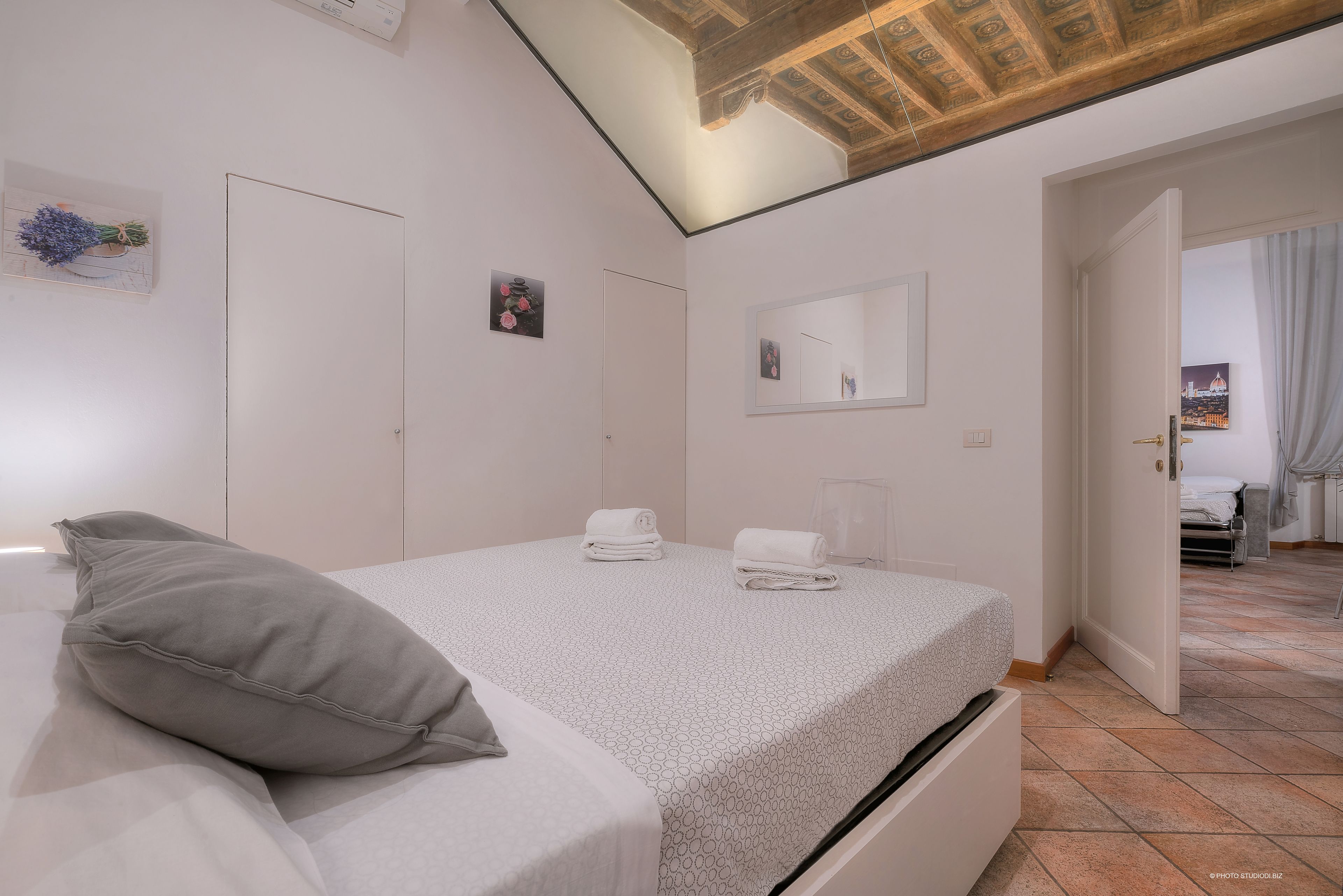 A bedroom with a bed, a nightstand, a mirror, and a door leading to another room.