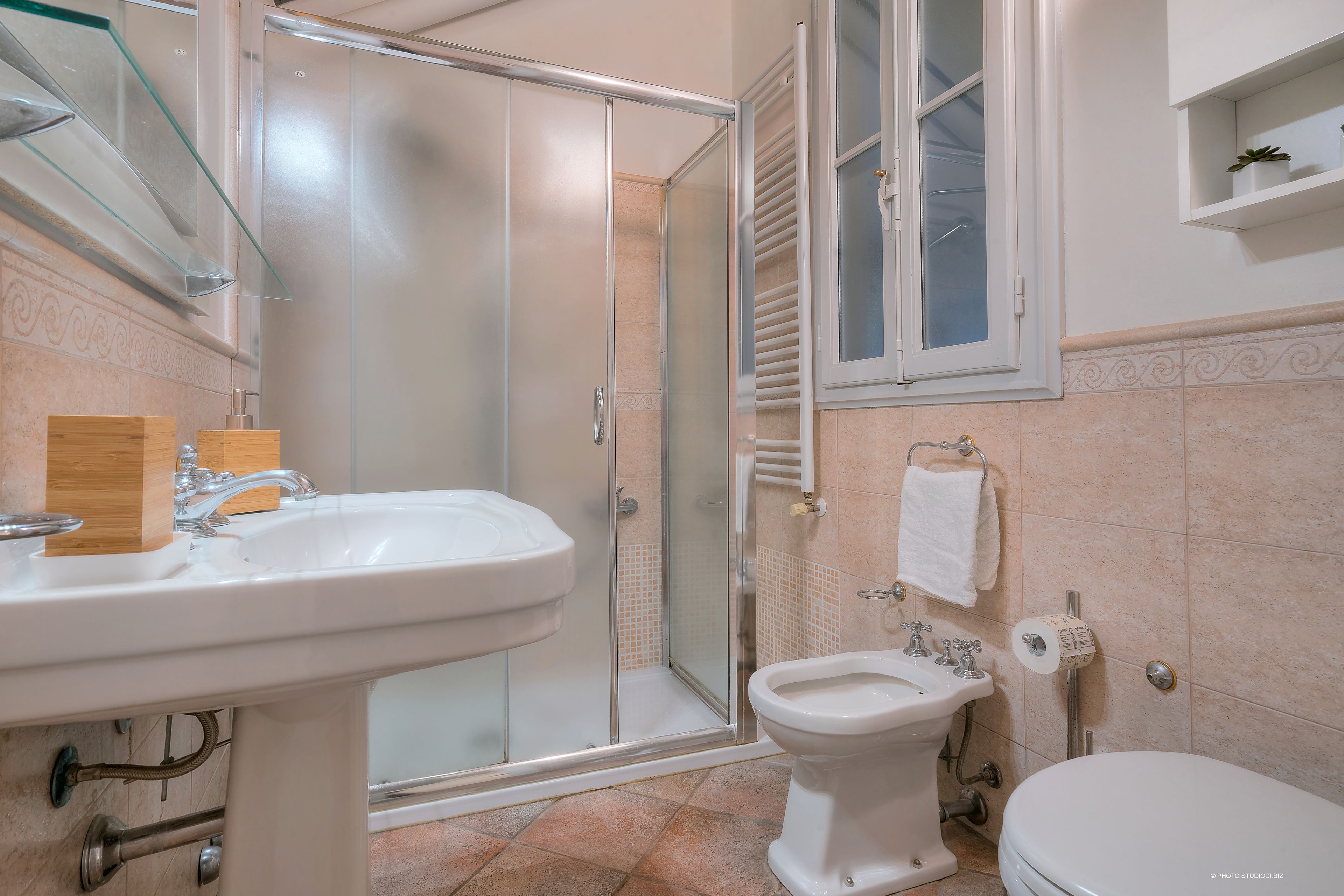 A bathroom with a glass-enclosed shower, a sink, a bidet, and a toilet.