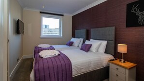 Een hotelkamer met twee bedden, een nachtkastje, een televisie en een raam met uitzicht op de stad.