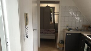 A narrow hallway with a wooden floor leading to a bedroom with a bed and a hanging light fixture. A kitchen area with a sink and cabinets is visible to the right. - 2 Zimmer Wohnung in Ludwigsburg Mitte (Ludwigsburg)