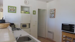 A kitchen with a sink, stove, microwave, and a small oven. There are green bowls on a shelf and a basket on the counter. - Villa with a stunning ocean view and a quiet, shaded terrace; air-conditioned bedrooms (La Croix-Valmer)
