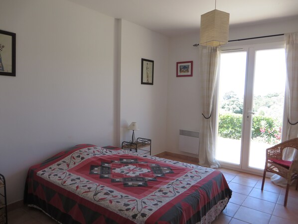 A bedroom with a bed, a chair, a lamp, and a window with curtains. - Villa with a stunning ocean view and a quiet, shaded terrace; air-conditioned bedrooms (La Croix-Valmer)