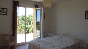A bedroom with a bed, a chair, a nightstand, and a window with curtains. - Villa with a stunning ocean view and a quiet, shaded terrace; air-conditioned bedrooms (La Croix-Valmer)