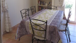 A dining area with a table set for four, surrounded by chairs, a bookshelf with books and decorative items, and a poster on the wall. - Villa with a stunning ocean view and a quiet, shaded terrace; air-conditioned bedrooms (La Croix-Valmer)