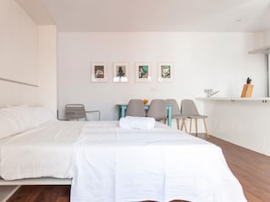Two single beds with white bedding, a desk, and a table, set against a minimalist backdrop with framed artworks on the wall.