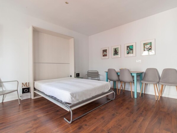 A modern, minimalist bedroom with a bed, a desk, and chairs.