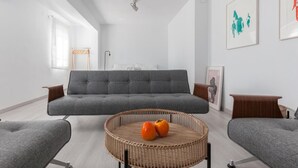 Ett modernt vardagsrum med en grå soffa, ett runt bord av rotting med två apelsiner på, och en grå fåtölj.