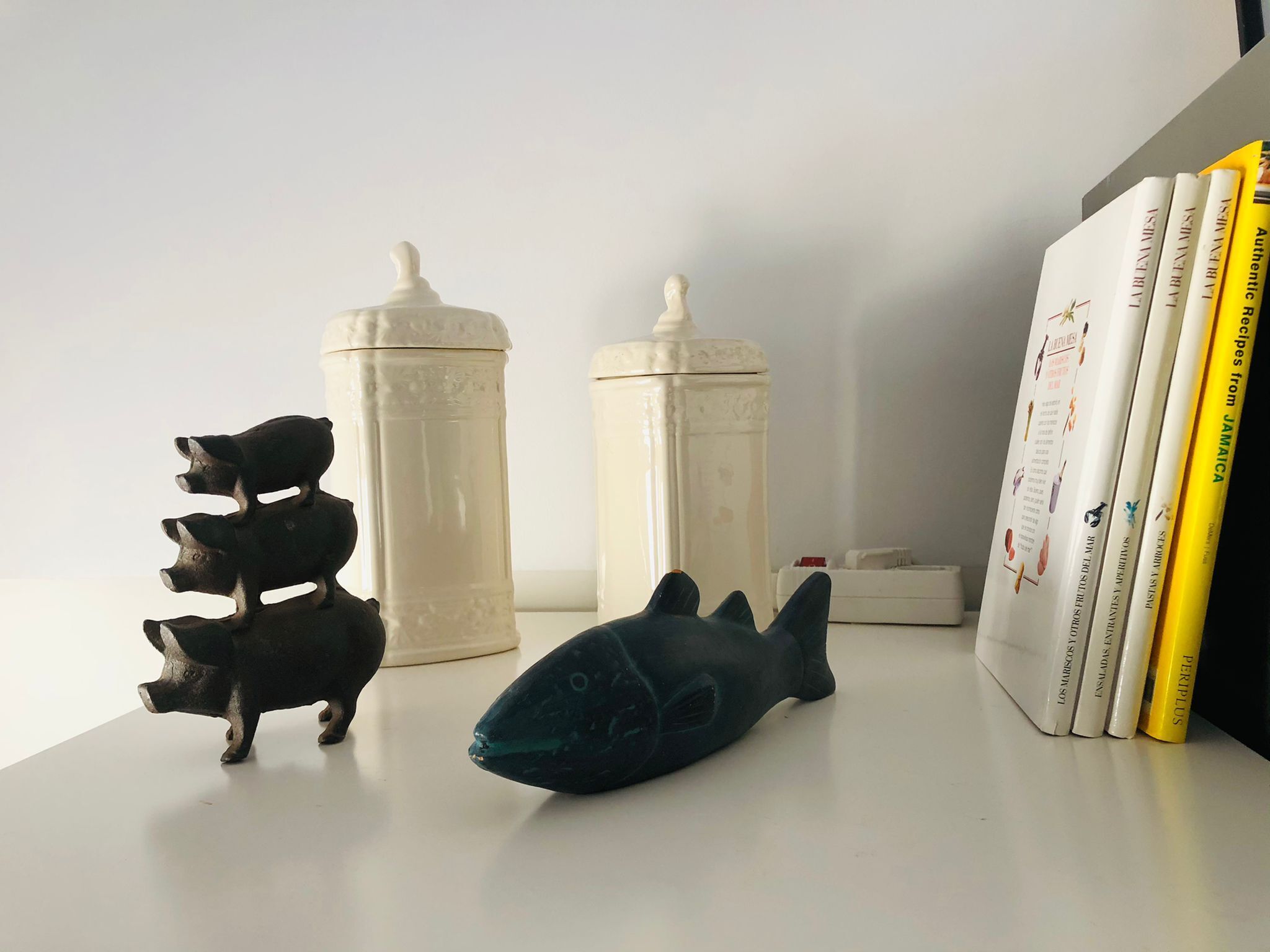 Uma prateleira comaturas de porco decorativas, uma escultura de peixe e uma fileira de livros.