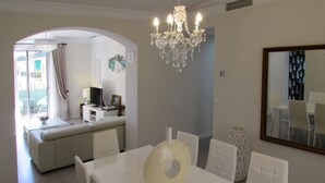Un coin repas avec une table et des chaises blanches, un lustre et un grand miroir au mur.