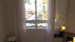 Une chambre d’hôtel avec un lit, une table de chevet avec une lampe, un miroir et une fenêtre avec des rideaux.