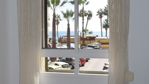 Une chambre avec une fenêtre donnant sur un parking et des palmiers, et des rideaux à la fenêtre.