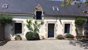 A stone building with two windows and a door, surrounded by greenery and a gravel driveway. - Gite sleeps 6 - heated indoor swimming pool (Évellys)