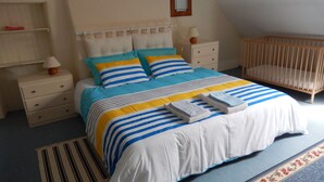 A bedroom with a bed, nightstands, a crib, and a mirror on the wall. - Gite sleeps 6 - heated indoor swimming pool (Évellys)