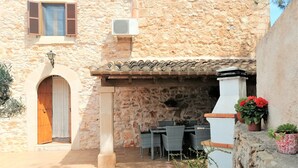 Un edificio de piedra con tejado de tejas, puerta de madera y un patio con mobiliario exterior.