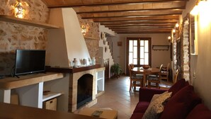 Una sala acogedora con chimenea de piedra, vigas de madera, un televisor y un sofá rojo.