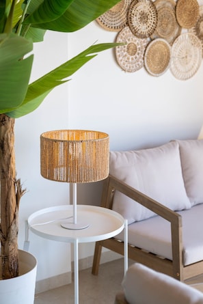 A round white table with a woven lamp, a potted plant, and a wall with woven wall art.
