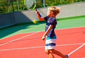 A tennis court with a player in mid-action, wearing a dark blue shirt and striped shorts.