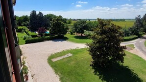 Une vue depuis un balcon donnant sur un jardin bien entretenu, avec un chemin de gravier, une pelouse soigneusement tondue et divers arbustes.