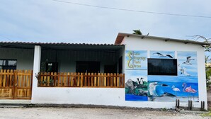 A building with a wooden fence, a sign reading "Casa Hospedaje Punta Arena," and a mural of birds and flamingos. - Casa Hospedaje Punta Arena (Puerto Villamil)
