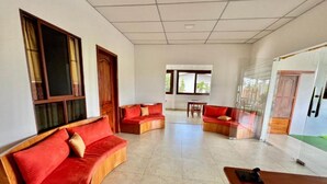 A spacious room with a wooden sofa set, a small table, and a glass door leading outside. - Casa Hospedaje Punta Arena (Puerto Villamil)