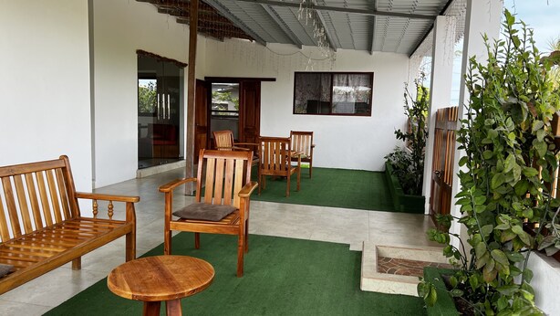 A covered outdoor seating area with wooden furniture and artificial grass. - Casa Hospedaje Punta Arena (Puerto Villamil)